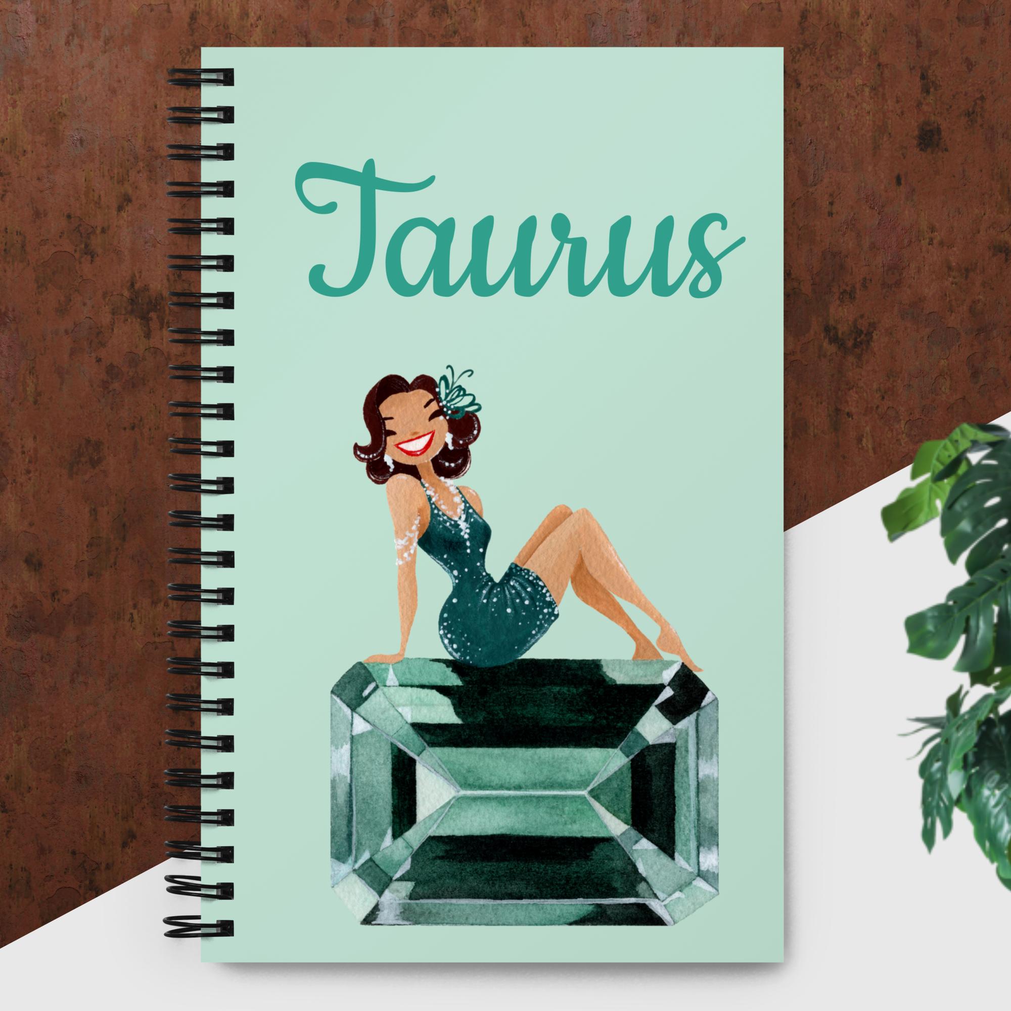 Blue/green notebook with an illustrated image of a glamorous brunette sitting on a gemstone with text displaying "Taurus" above